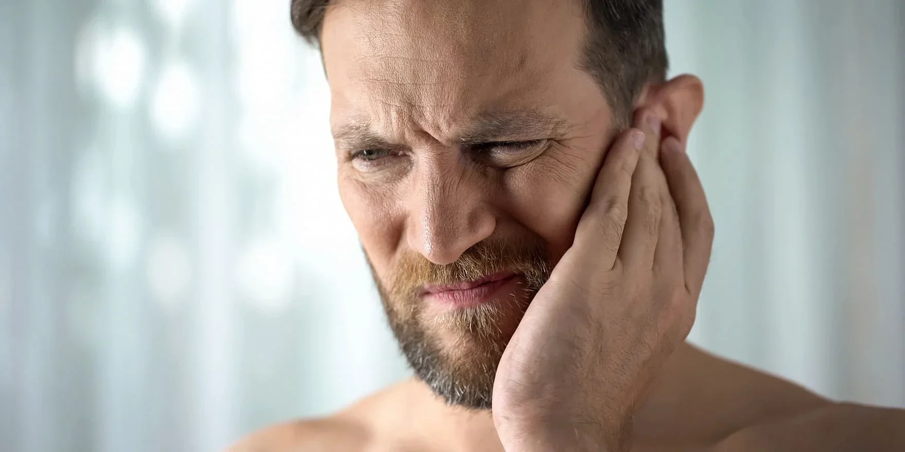 Mann mit Tinnitus hält sich das Ohr