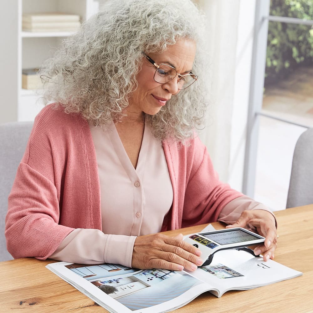 Dame liest mit mobilem digitalem Lesegerät Zeitung. Vergrößernde Sehhilfen von Optiker Gronde