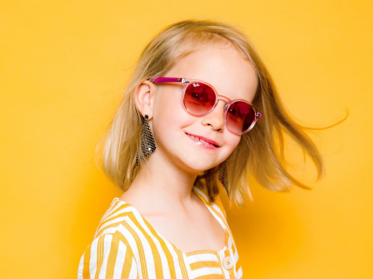 Mädchen in Gelb trägt pinke Ray-Ban Sonnenbrille für Kinder von Gronde Sehen und Hören
