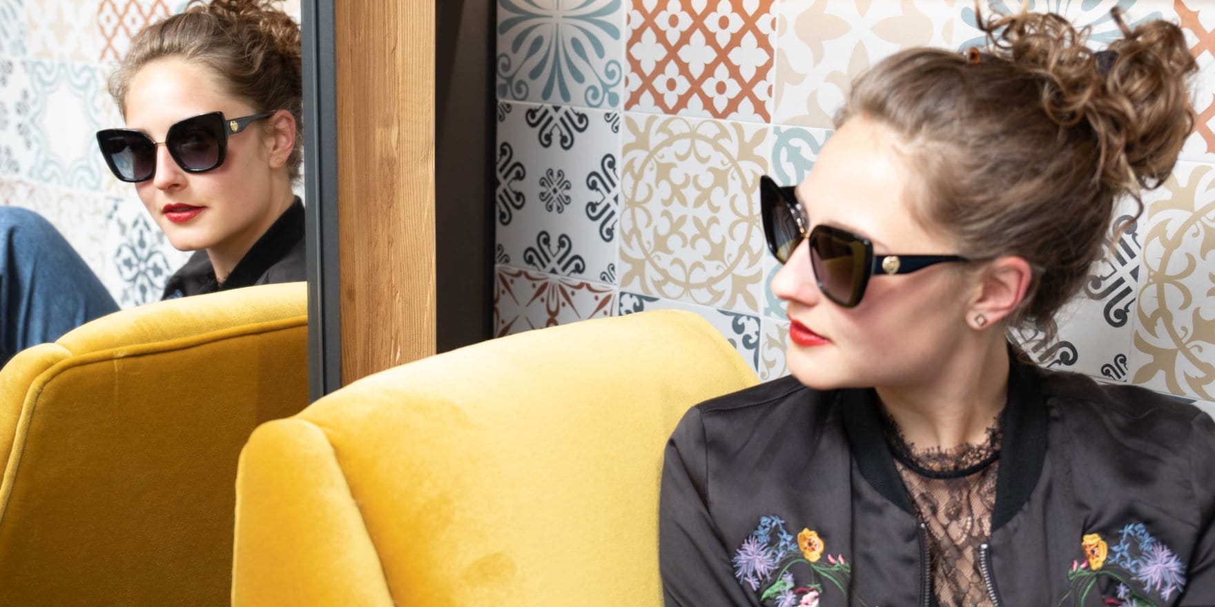 Sonnenbrillen mit Sehstärke: Junge Frau mit Dutt und schwarzer Dolce&Gabbana Sonnenbrille mit Sehstärke von Optiker Gronde sieht sich im Spiegel an