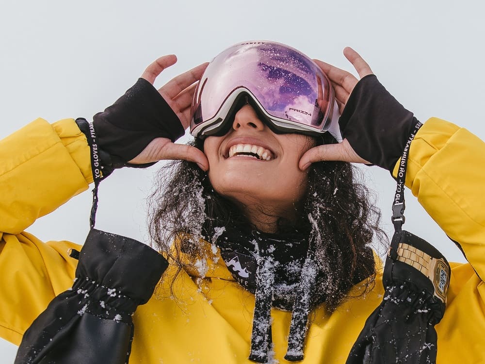 Junge Frau mit Skibrille von Optiker Gronde und gelbem Overall im Schnee