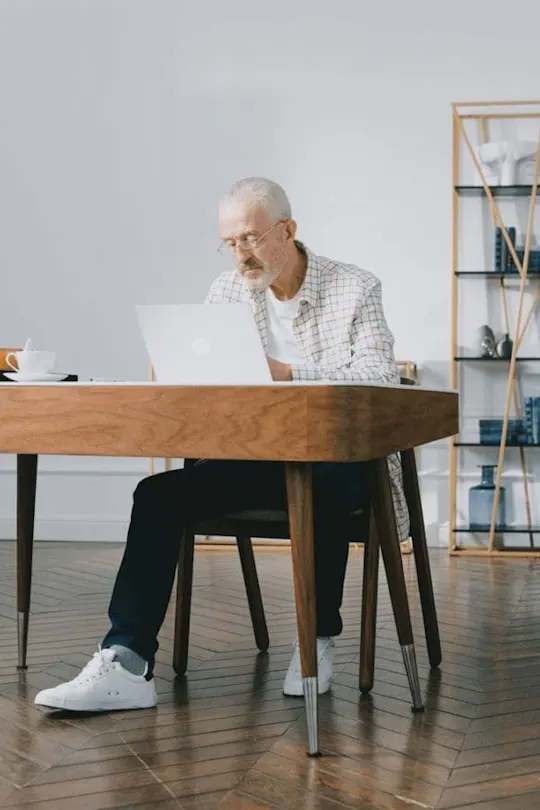 Älterer Mann mit Brille sitzt an einem Schreibtisch vor dem PC