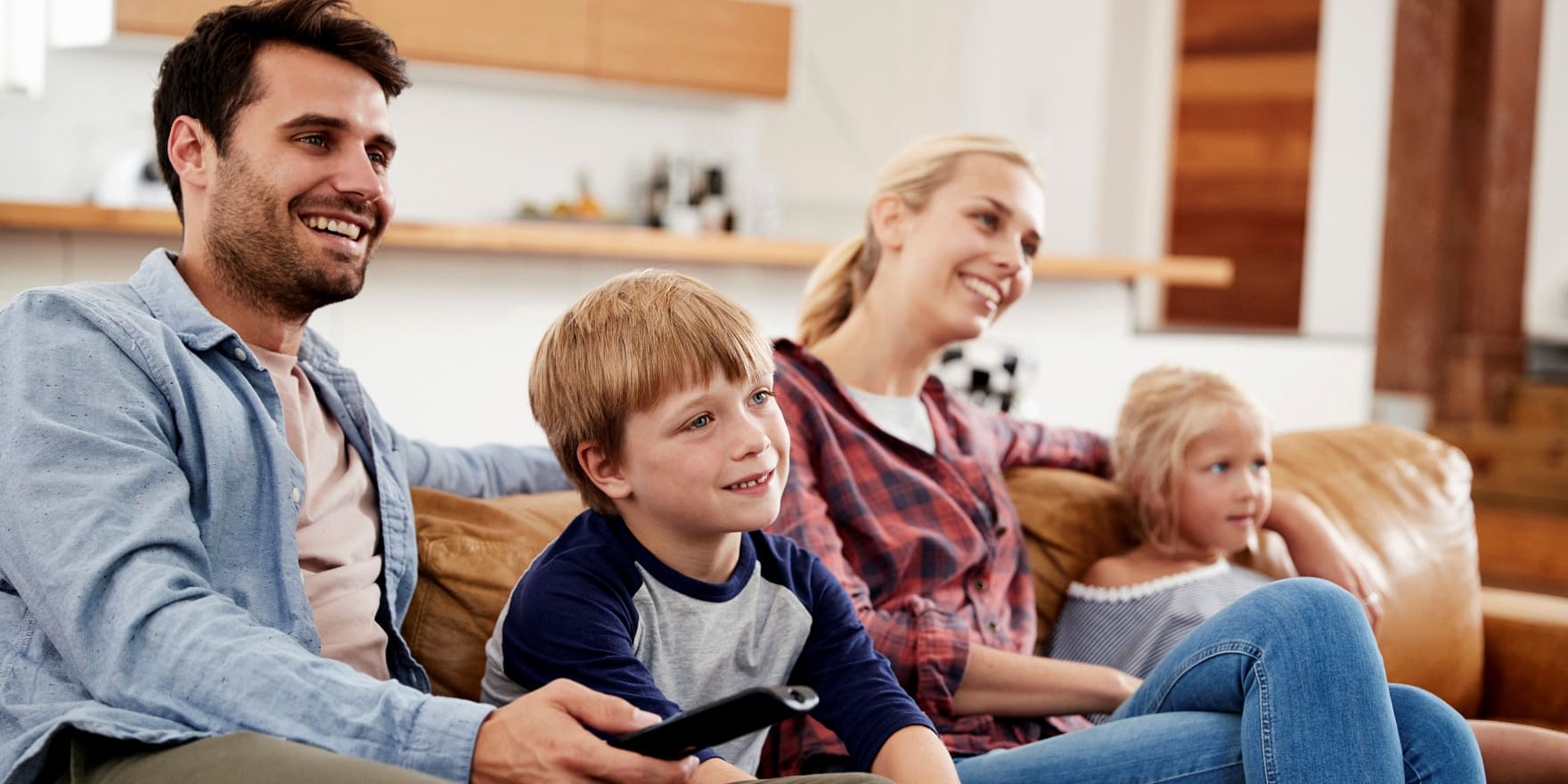 Junge Familie vorm Fernseher, er mit Hinter-dem-Ohr-Hörgerät zum Nulltarif von GRONDE