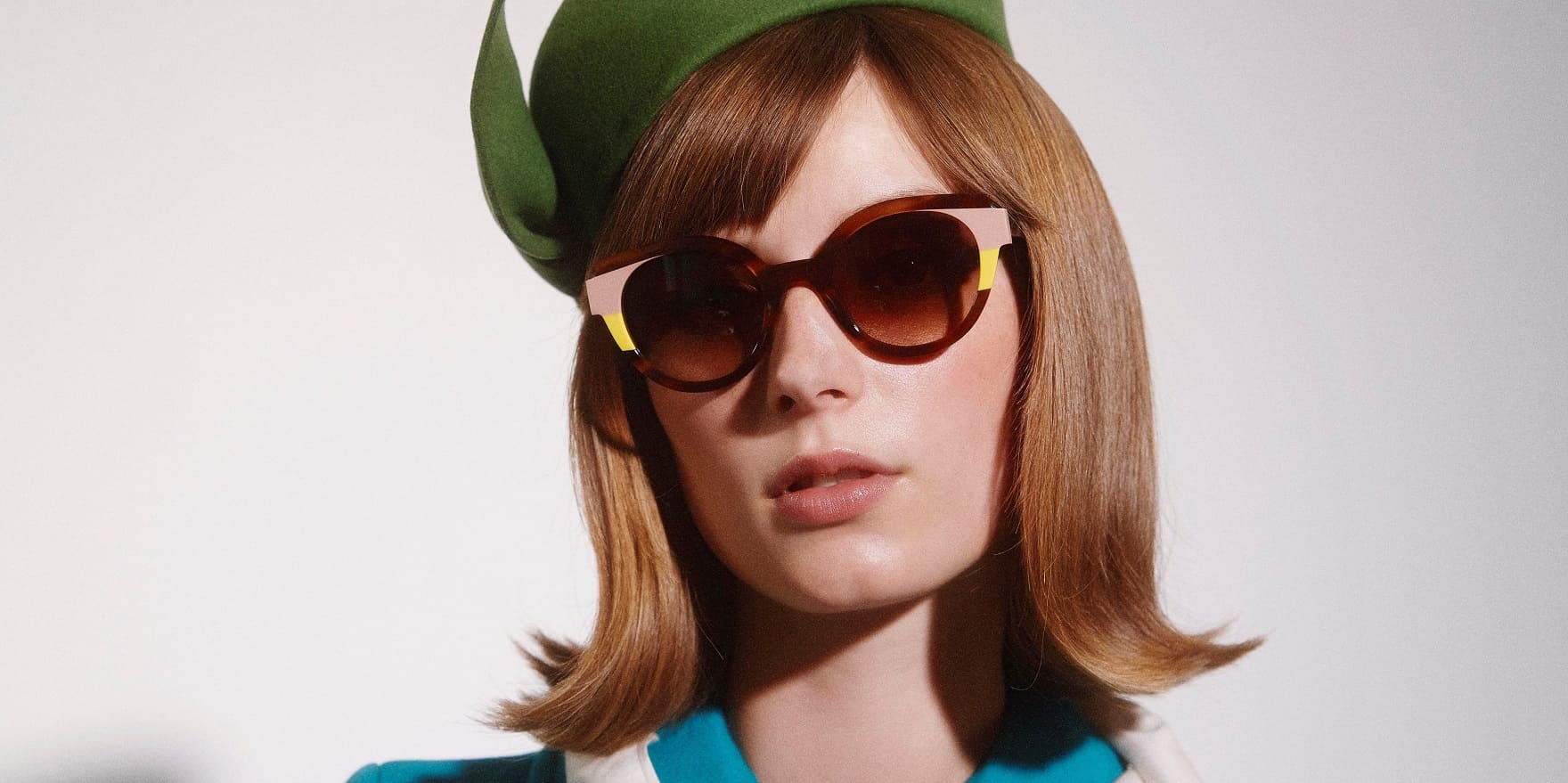 Junge Frau mit grünem Hut und bunter Brille präsentiert die Brillen Trends 2023 im Blog von Optiker Gronde