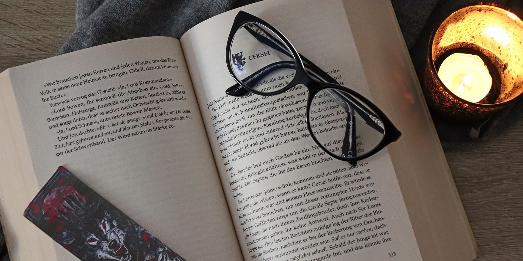 Lesebrille von Optiker Gronde auf aufgeschlagenem Buch mit Teelicht