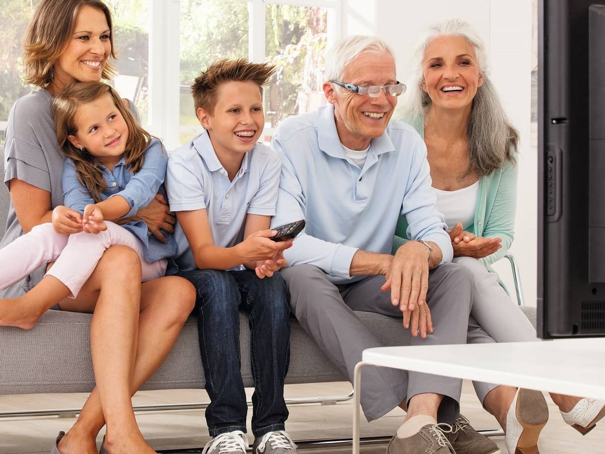 Älterer Herr mit Fernseh-Brille und seiner Familie vorm Fernseher. Vergrößernde Sehhilfen von Optiker Gronde