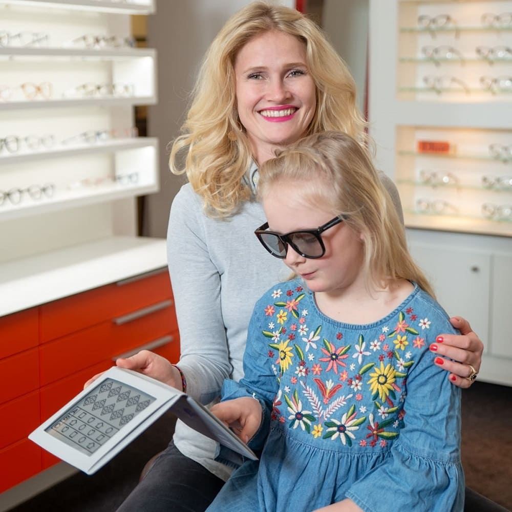 Kinder-Optometrie bei Optiker Gronde. Junge, blonde Optikerin mit Mädchen mit SpezialbrilleSpezial
