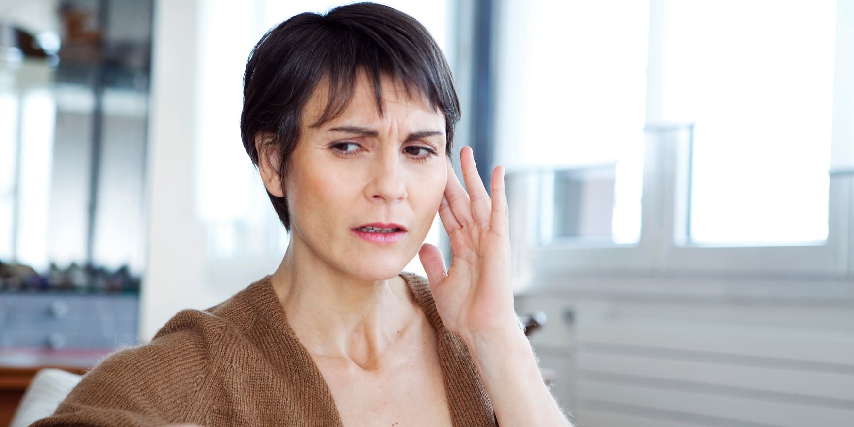 Frau greift sich irritiert ans Ohr. Braucht Tinnitus-Therapie bei Hörakustik Gronde