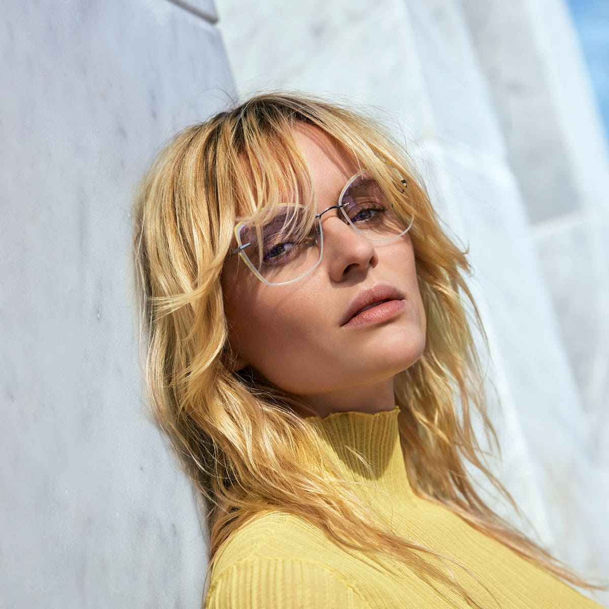 Blonde Frau mit gelbem Shirt und beiger, großer, ultra-leichter Silhouette Brille TMA LaLigne von Optiker Gronde
