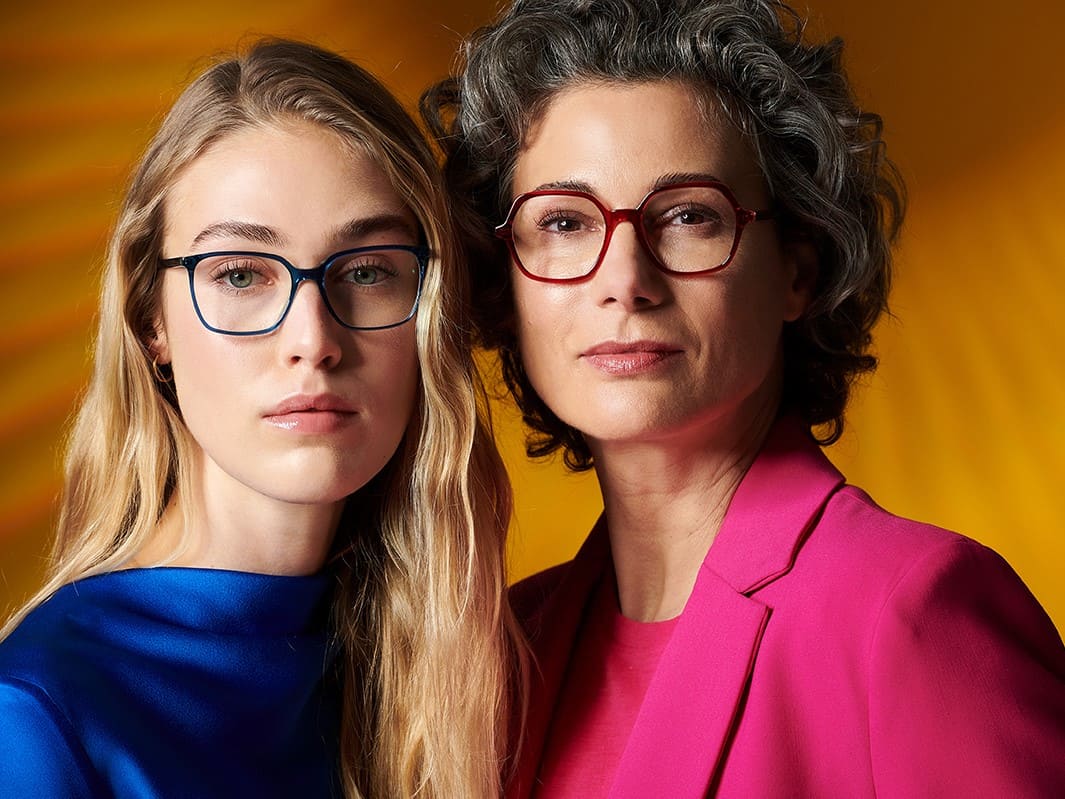 Zwei Frauen mit Colibris Brillen aus Acetat von Optiker Gronde, Augsburg. Links Blondine mit Blauer Eva 133, rechts graumelierte schöne Dame mit Edda 132